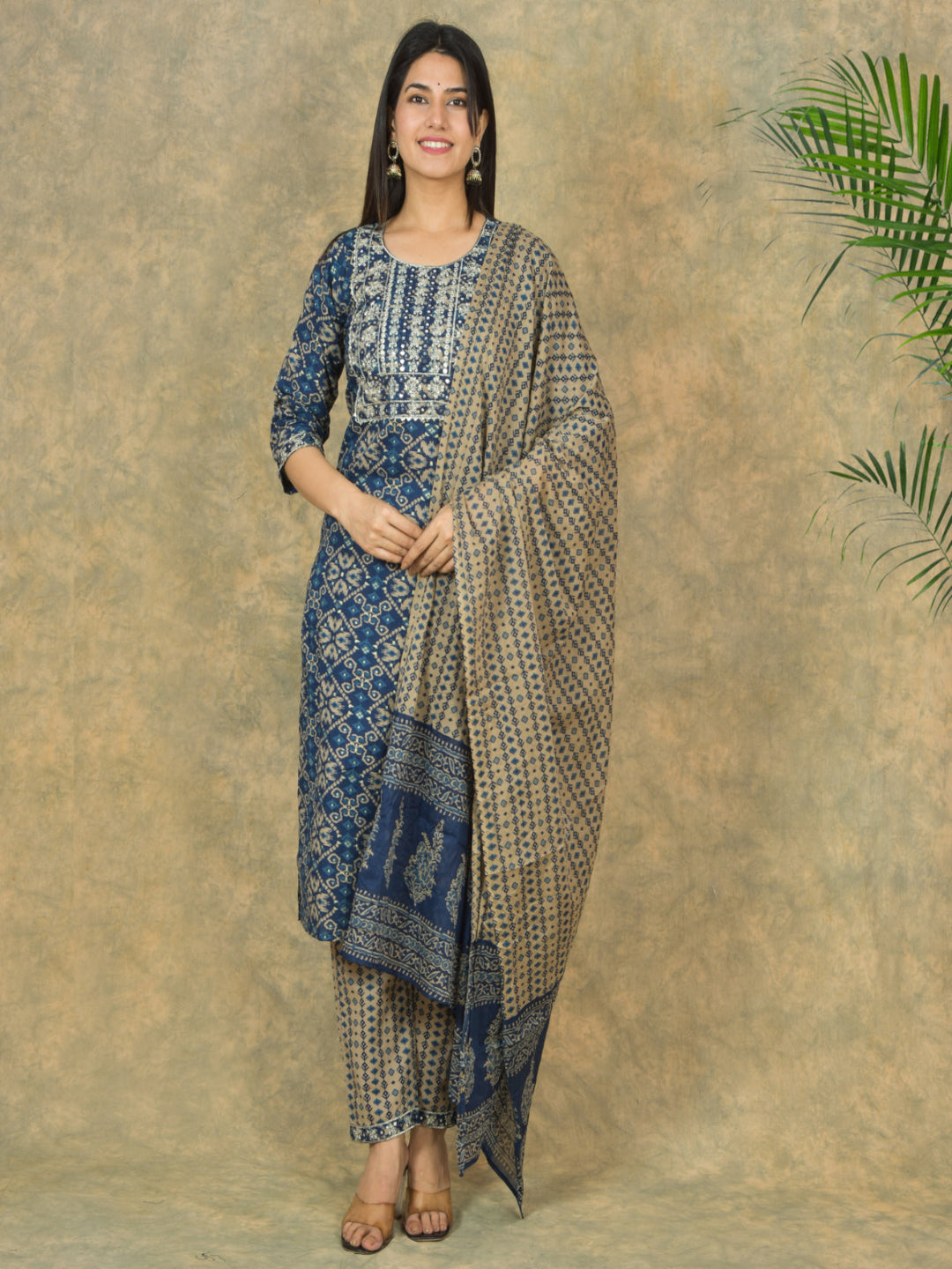 Woman wearing a blue and beige patterned outfit with a matching scarf against a textured beige background.