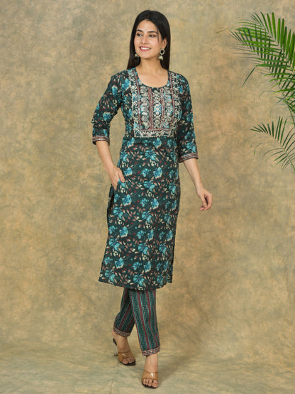 Woman wearing a floral kurta with pants against a textured wall.