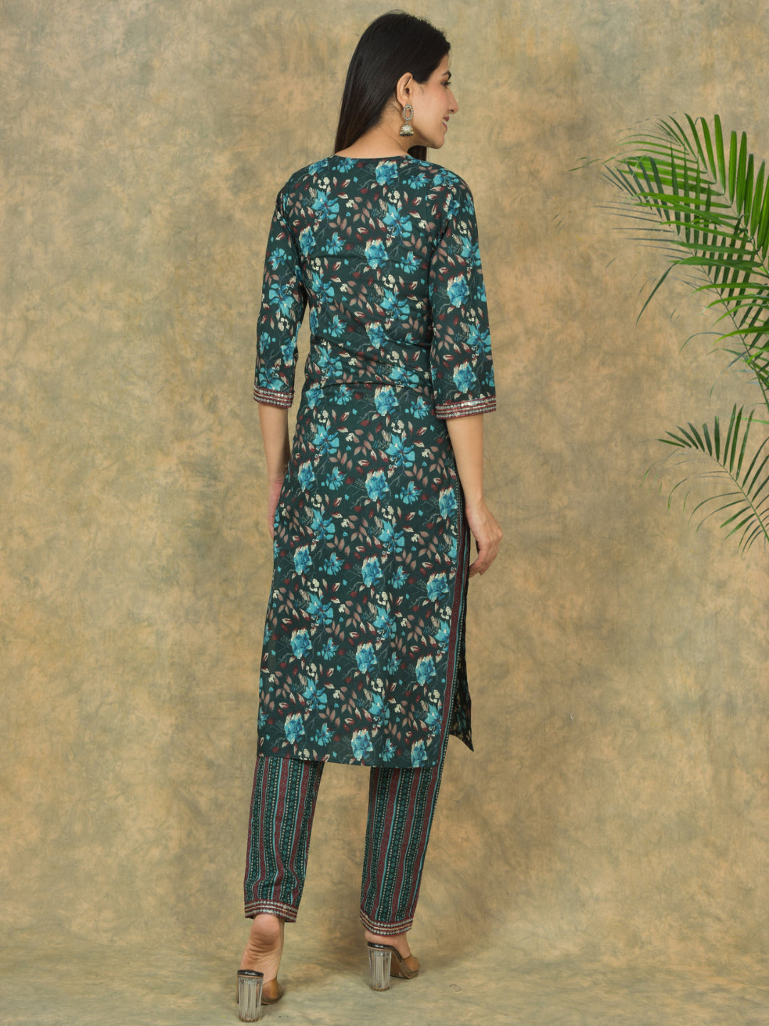Woman wearing a floral kurta with pants against a textured beige wall.