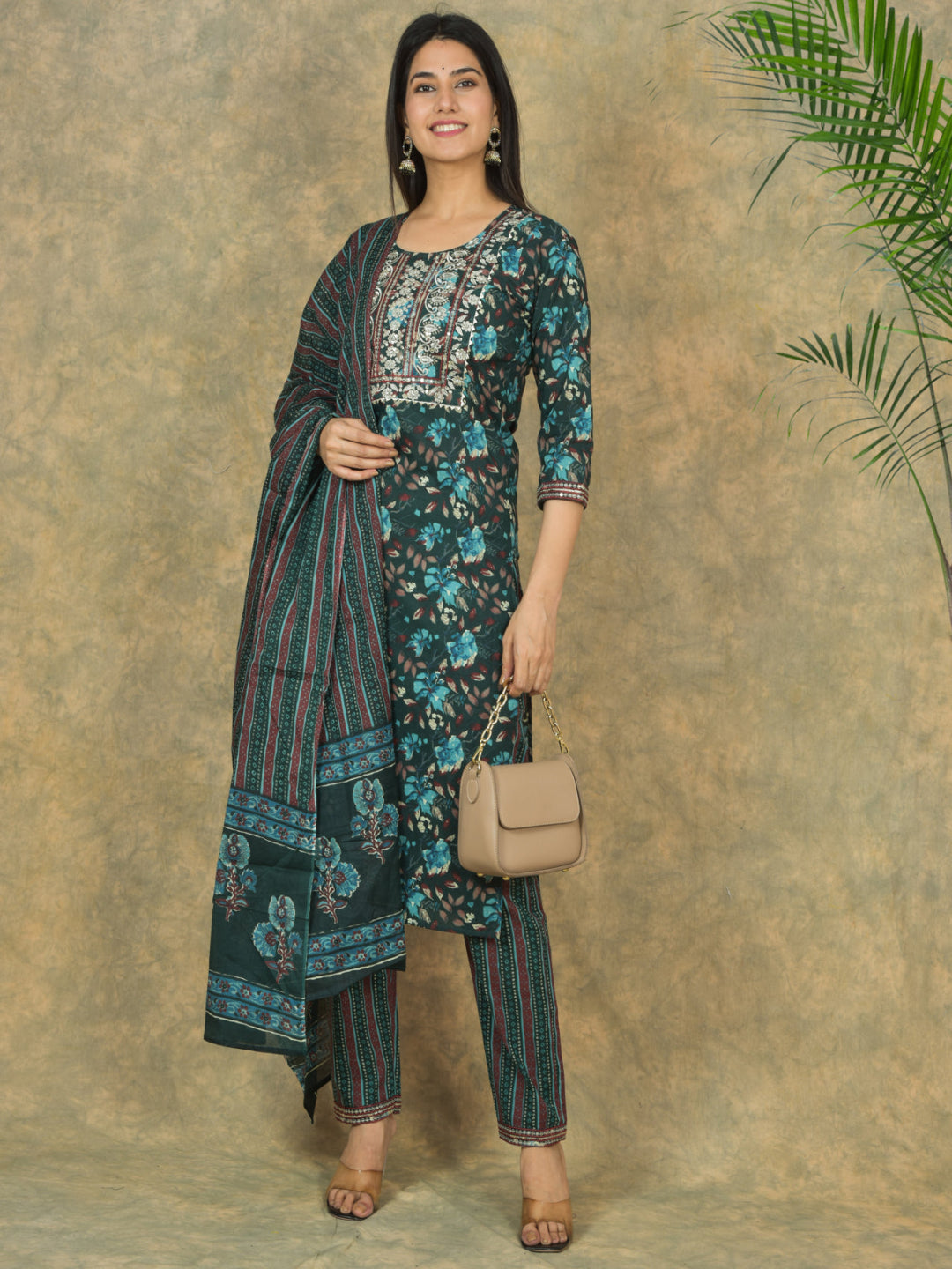Woman wearing a floral outfit with a beige handbag against a textured wall.