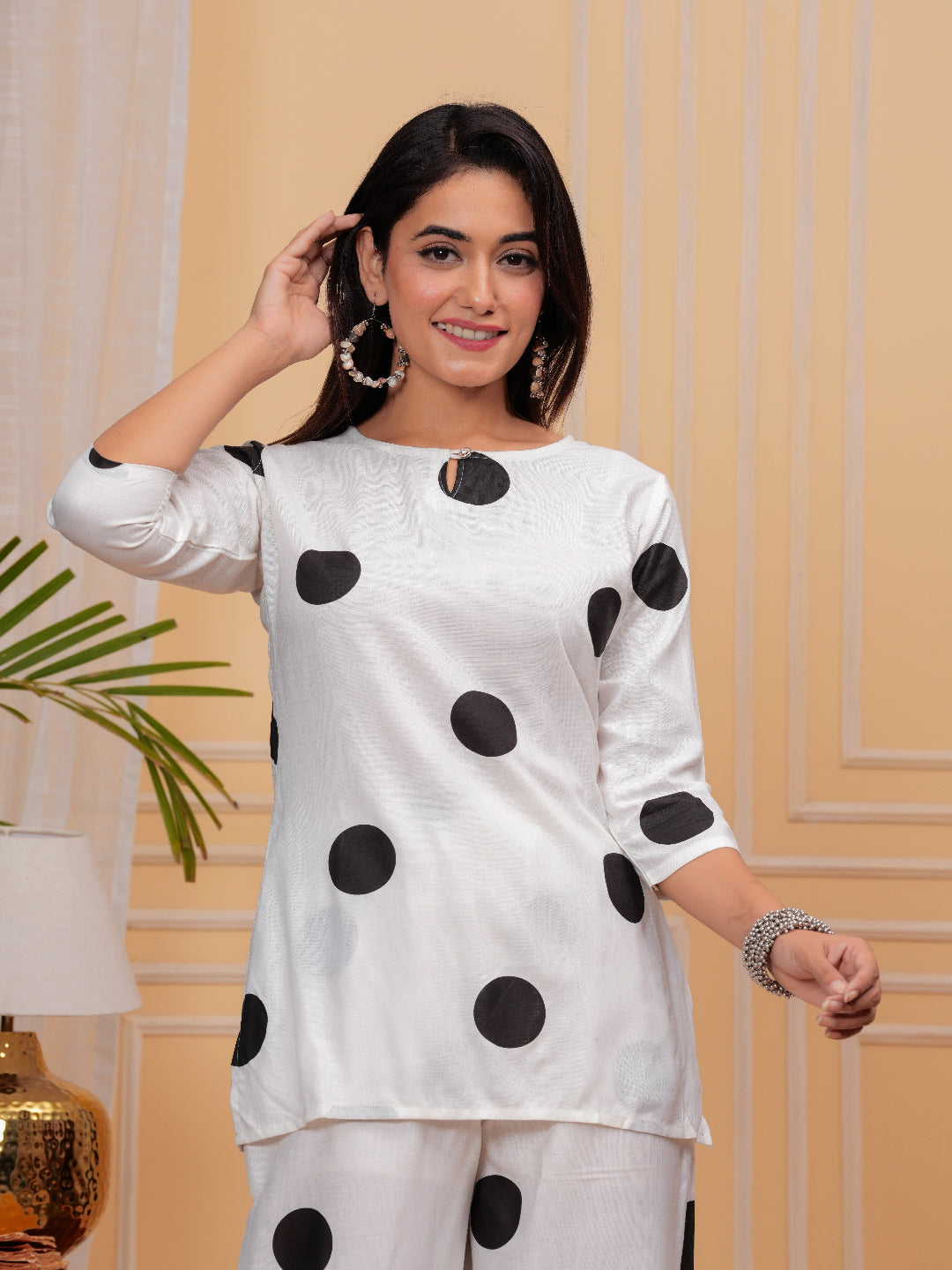 Woman wearing a white outfit with black polka dots against a beige wall.
