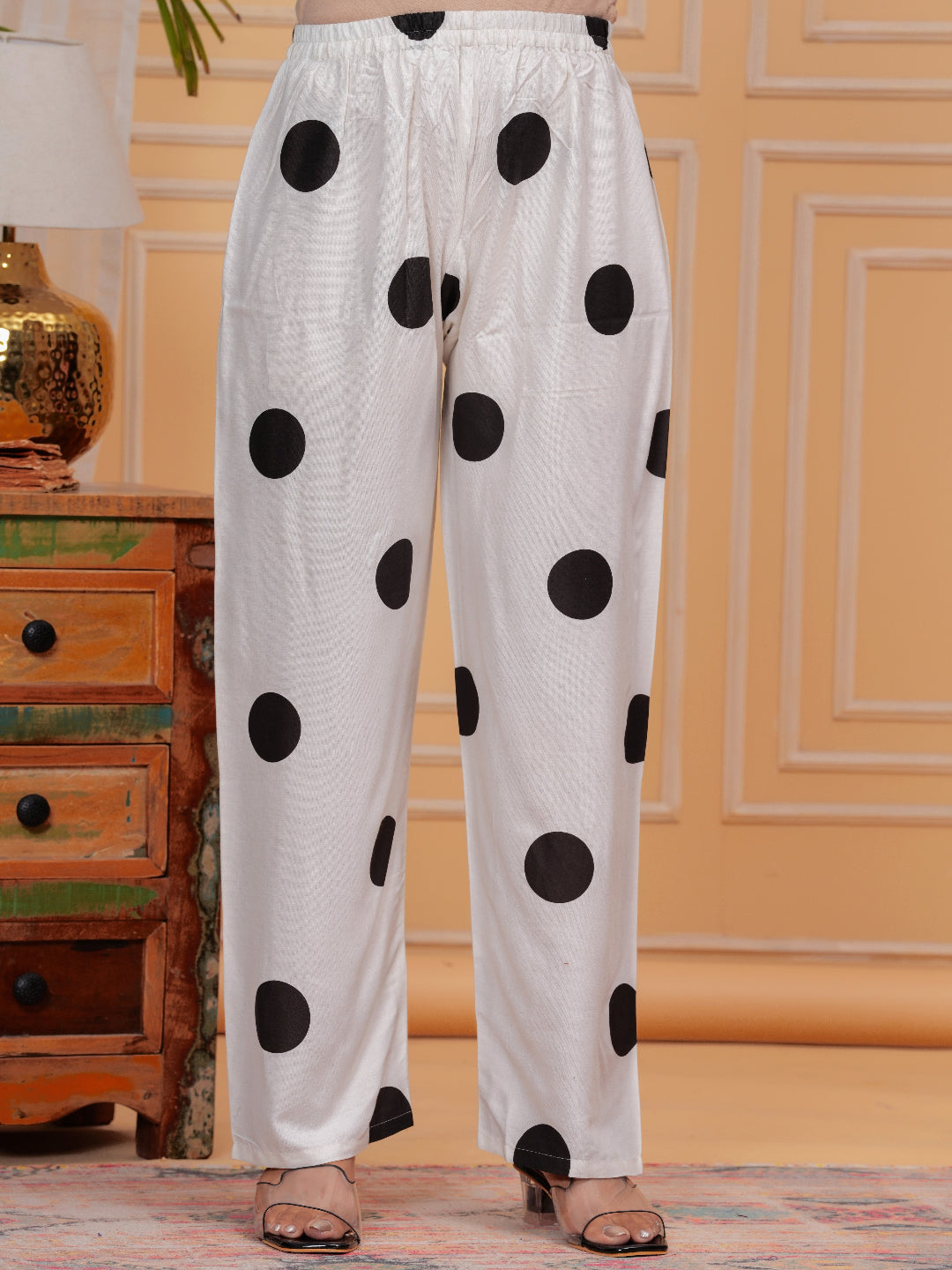 White pants with black polka dots worn by a person in a room with a wooden dresser and decorative items.