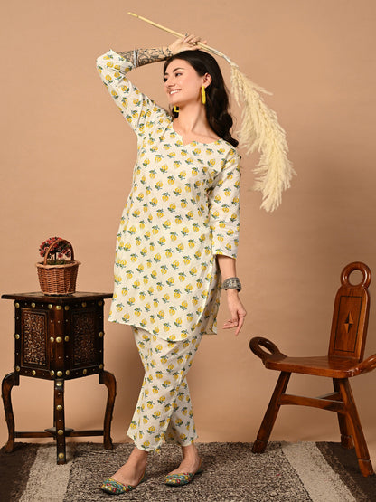 Woman in a yellow and white patterned outfit standing in a room with wooden furniture.