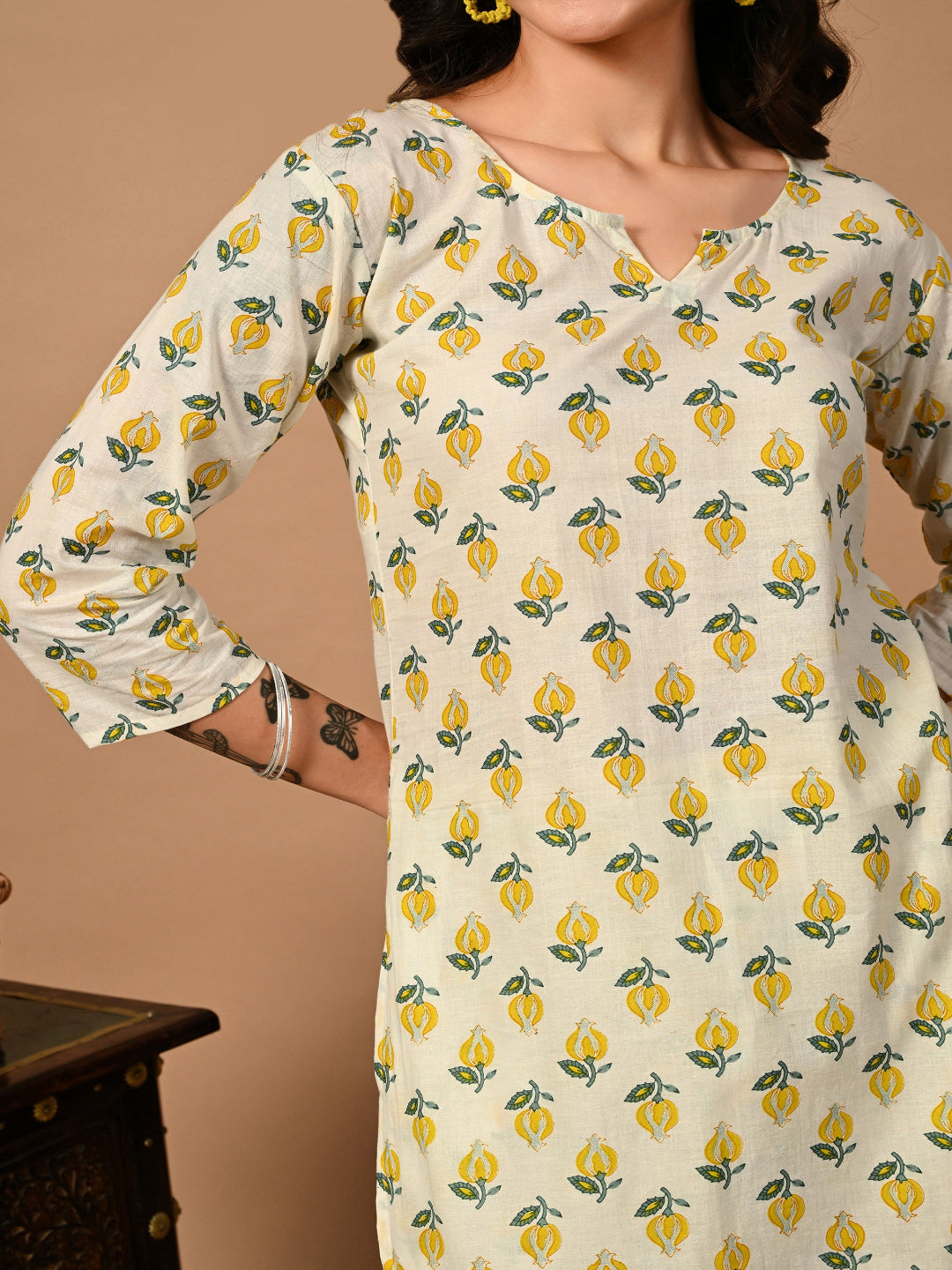 Woman wearing a white kurta with yellow floral pattern against a beige background